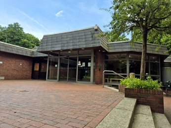 Außenansicht Eingang Hallenbad Barrierefreier Eingang eines backsteingebauten Gebäudes, umgeben von grünen Bäumen.