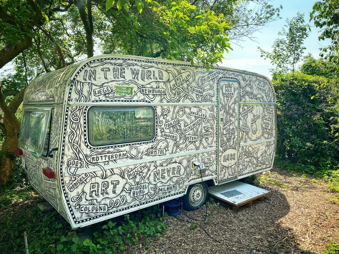 Erbsen im Grünen verweilt ein künstlerisch bemalter, detailreich verzierter Wohnwagen.