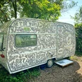 Erbsen im Grünen verweilt ein künstlerisch bemalter, detailreich verzierter Wohnwagen.