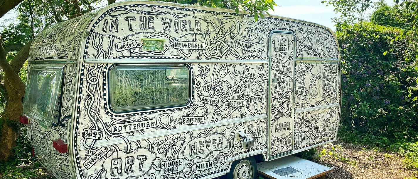 Erbsen im Grünen verweilt ein künstlerisch bemalter, detailreich verzierter Wohnwagen.