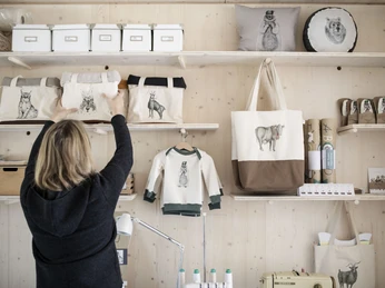 karlmeise Frau ordnet handgefertigte Taschen mit Tiermotiven auf Holzregalen.