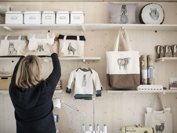 karlmeise Frau ordnet handgefertigte Taschen mit Tiermotiven auf Holzregalen.