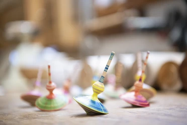 Holzdesign Eva Engler Mehrere bunte Kreisel aus Holz stehen auf einem Tisch in einem Handwerksatelier.