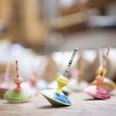 Holzdesign Eva Engler Mehrere bunte Kreisel aus Holz stehen auf einem Tisch in einem Handwerksatelier.
