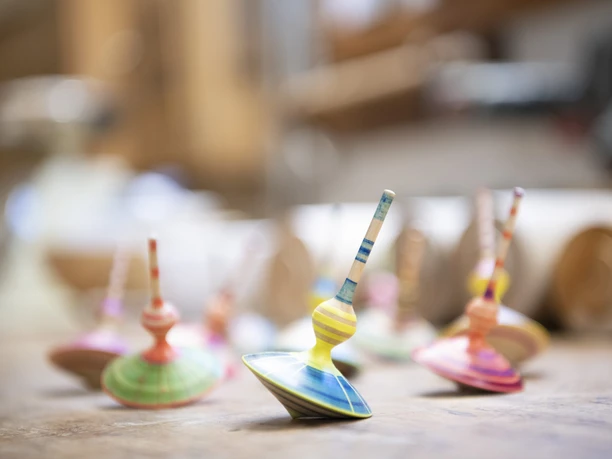 Holzdesign Eva Engler Mehrere bunte Kreisel aus Holz stehen auf einem Tisch in einem Handwerksatelier.