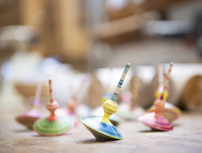 Holzdesign Eva Engler Mehrere bunte Kreisel aus Holz stehen auf einem Tisch in einem Handwerksatelier.