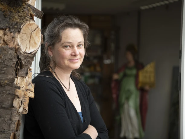 Hinterglasmalerei Dichtl Eine Frau steht an der Werkstatttür, eine bemalte Figur ist im Hintergrund.