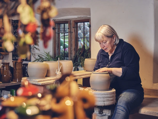 Hafnerei Glentleiten Eine Frau töpfert konzentriert an einem Keramiktisch in einer Werkstatt.
