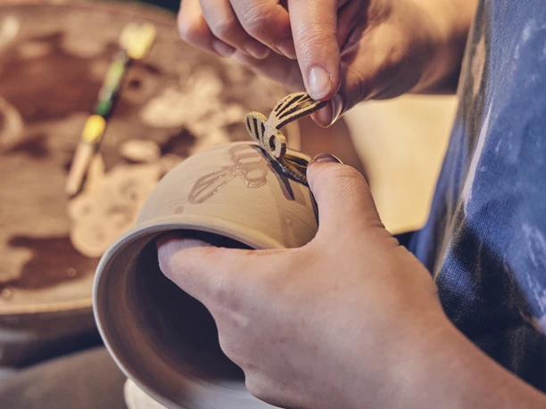 Hafnerei Glentleiten Eine Person verziert mit präzisem Handwerk eine tönerne Schale.