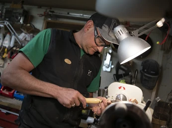 Da Doni Handwerker in Werkstatt drechselt Holz auf einer Maschine unter einer Lampe.