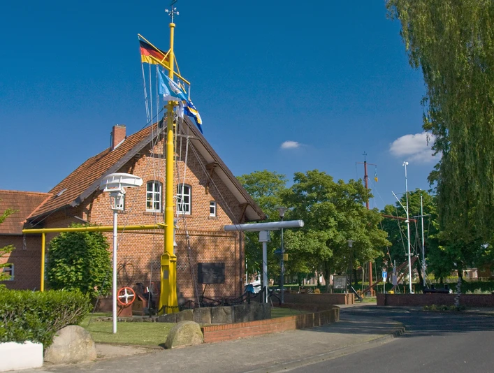 Backsteingebäude mit Schiffsmodellen, Masten und Flaggen unter blauem Himmel in Haren an der Ems.