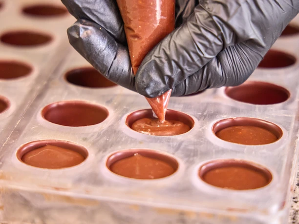Chocowerk Wallgau Herstellung von Pralinen in einer Form mit Kakaomasse aus einer Spritztüte.