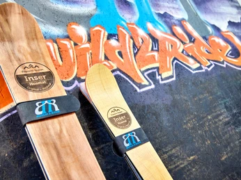 Build2Ride Zwei Holzski vor einer farbenfrohen Graffiti-Wand mit dem Schriftzug „Build2Ride“.