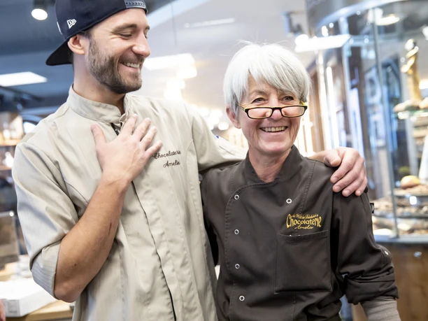 Chocolaterie Amelie Zwei Personen lächeln in einer Chocolaterie, beide tragen Schürzen.