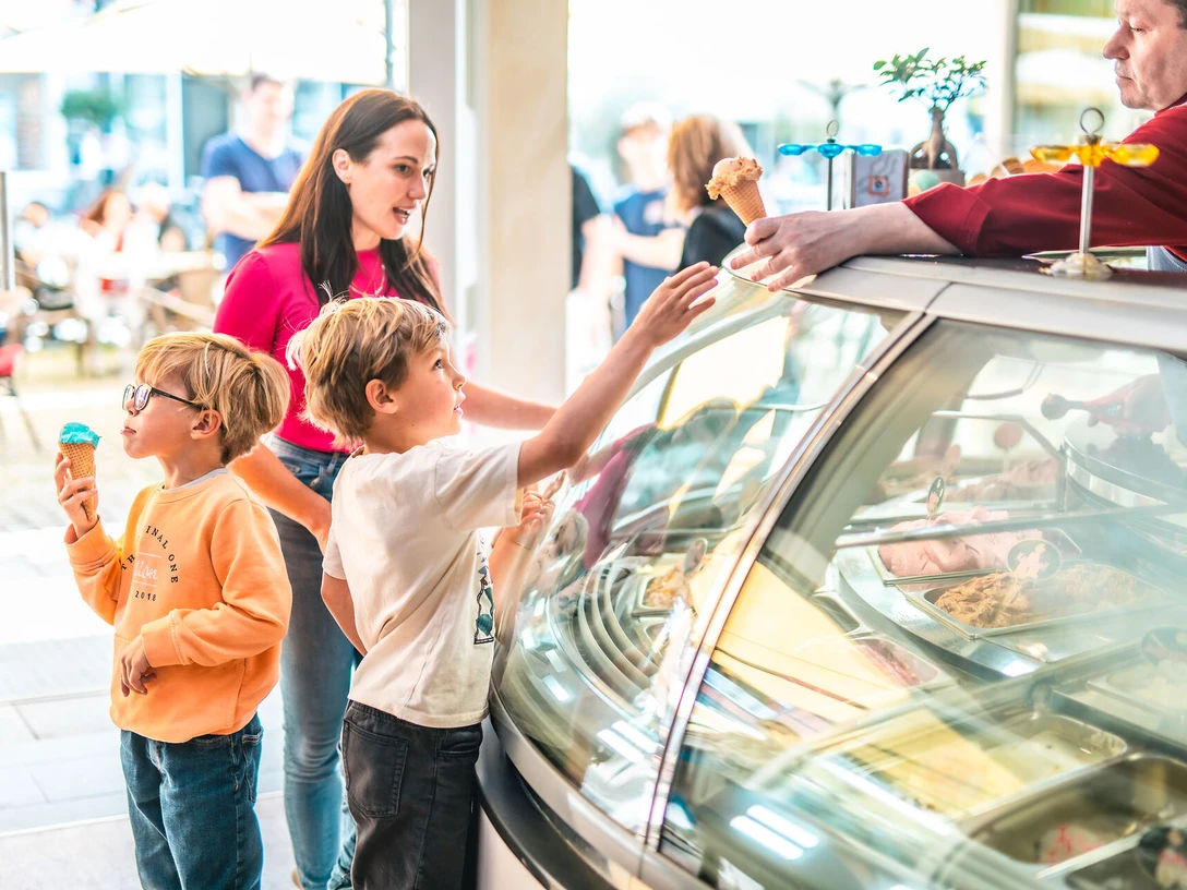 Genießen Sie köstliches Eis im Eiscafé Arte Dolcelle in Celle Zwei Kinder und eine Frau stehen an der Theke des Eiscafés Arte Dolcelle in Celle und genießen leckere Eistüten, während ein Mitarbeiter ihnen Eis serviert.