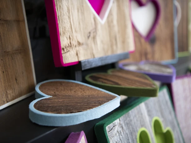 Alpenterieur Herzförmige Holzkunstwerke mit bunten Filzrändern an einer Wand in einem Geschäft.