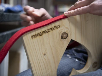 Alpenterieur Eine Hand bearbeitet ein Holzstück mit rotem Filz, graviert mit "Alpenterieur".