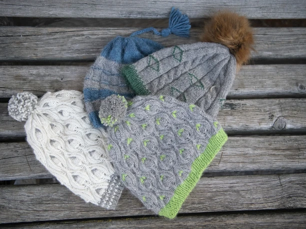 Alpakahof Riegsee Verschiedene gestrickte Mützen liegen auf einem Holztisch; jede hat ein eigenes Design.