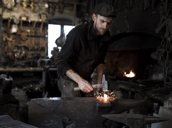 Aberl Metallgestaltung Ein Schmied arbeitet konzentriert am Amboss, umgeben von Werkzeugen.