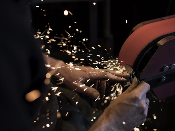 Aberl Metallgestaltung Ein Schleifgerät erzeugt Funken, während Metall bearbeitet wird. Hände sind im Fokus.
