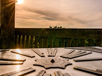 Ein hölzerner Aussichtsturm mit Orientierungstafel im Sonnenuntergang, umliegende Landschaft sichtbar.