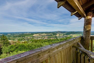 Luisenturm_pro Wirtschaft GT_Mario Wallenfang (3).jpeg Blick von einem hölzernen Aussichtsturm auf eine weitläufige grüne Hügellandschaft und Dörfer.