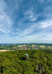 Borgholzhausen-Luisenturm-Teutoburger-Wald-Tourismus-D-Ketz-059.jpg Landschaft mit bewaldetem Hügel, darüber ein hoher Turm, im Hintergrund weite Felder und blauer Himmel.