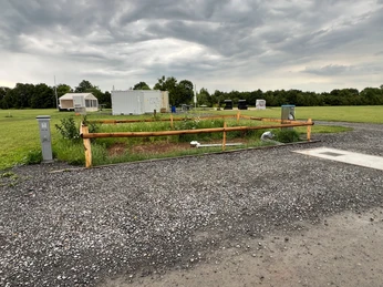 WoMo Weser-Ufer-Urlaub Ein Wohnmobilstellplatz mit Stromanschlüssen und Grünfläche bei bewölktem Himmel am Weserufer.