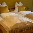 Schlafzimmer Gästehaus Reichmann Zwei Einzelbetten mit blassgelben Decken und dekorativen Kissen vor einer warmen, gelben Wand.