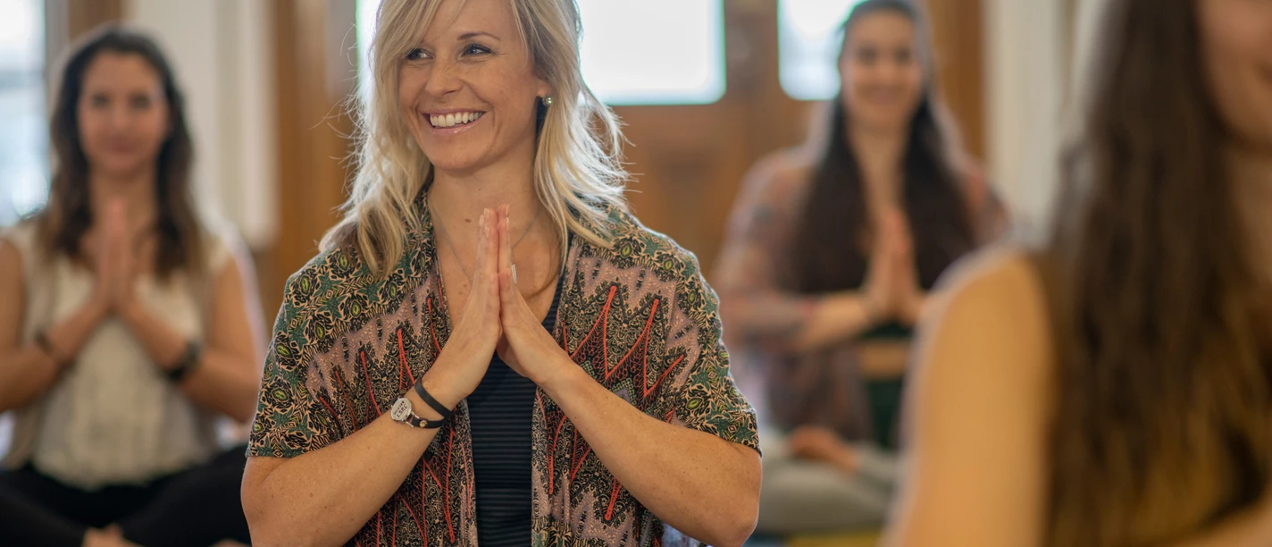 Sonntagsyoga Lächelnde Frauen üben im hellen Raum Yoga im Schneidersitz mit gefalteten Händen.