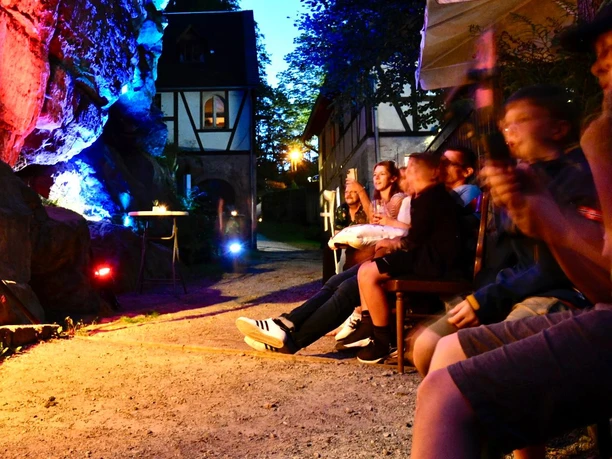 Freunde genießen abends ein bunt beleuchtetes Ambiente im Biergarten neben historischer Fachwerkarchitektur.