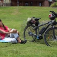 Eine Frau und ein Mann relaxen auf einer Wiese neben ihrem E-Bike in einer grünen Umgebung.