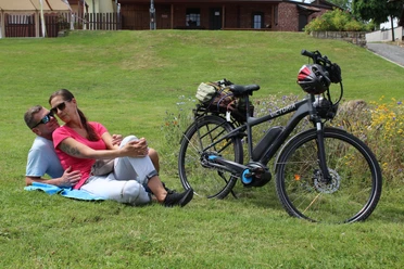 Radfahren in der Mittelweser-Region Eine Frau und ein Mann relaxen auf einer Wiese neben ihrem E-Bike in einer grünen Umgebung.
