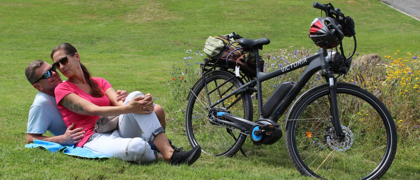 Radfahren in der Mittelweser-Region Eine Frau und ein Mann relaxen auf einer Wiese neben ihrem E-Bike in einer grünen Umgebung.