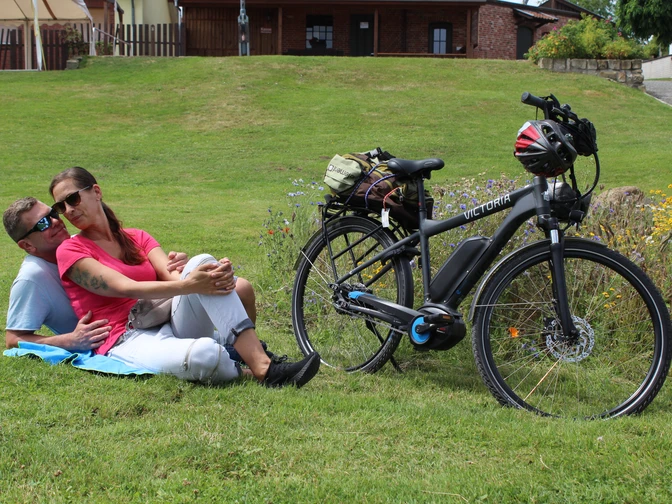 Radfahren in der Mittelweser-Region Eine Frau und ein Mann relaxen auf einer Wiese neben ihrem E-Bike in einer grünen Umgebung.A woman and a man relax on a meadow next to their e-bike in a green setting.En kvinde og en mand slapper af på en eng ved siden af deres elcykel i grønne omgivelser.Een vrouw en een man ontspannen op een weiland naast hun e-bike in een groene omgeving.