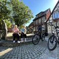 Zwei Frauen sitzen auf einer Mauer vor dem Spargelbrunnen in Nienburg, umgeben von Fachwerkhäusern.