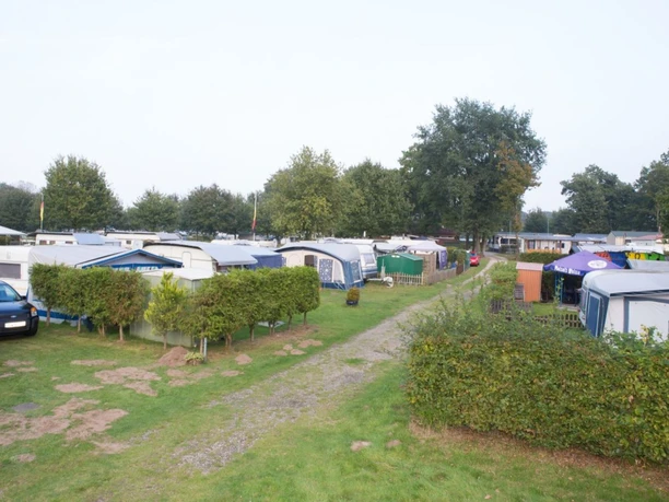Campingplatz Lathener Marsch.jpg Reihen von Wohnwagen mit Vorzelten auf gepflegtem Rasen, umgeben von Bäumen und Hecken.