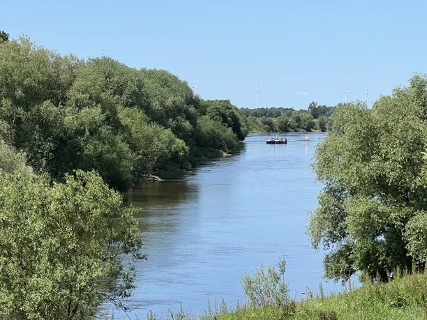 Breiter Flusslauf der Weser nahe Drakenburg, gesäumt von Bäumen und einem fernen Schiff am Horizont.