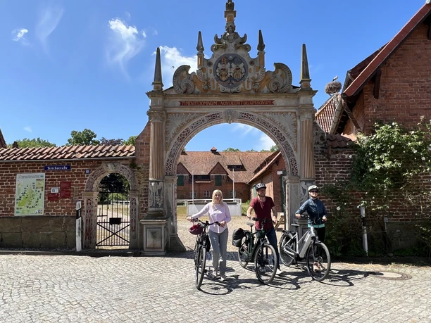 Drie mensen op fietsen staan voor een sierlijke boog uit de Wezerrenaissance.