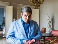 Ein gut gekleideter Mann in einem eleganten, historischen Raum mit kunstvollen Dekorationen.