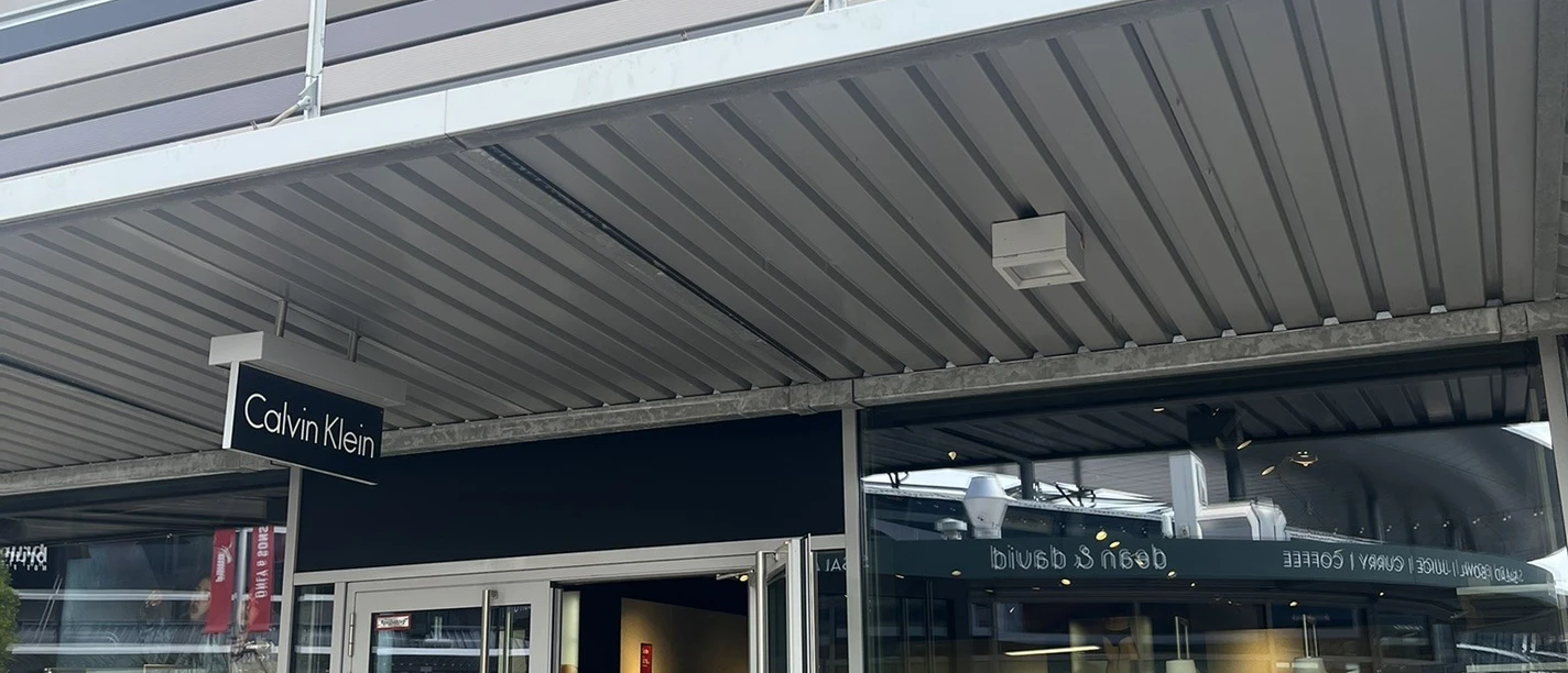Calvin Klein.jpg Das Bild zeigt einen modernen Calvin Klein Store mit geöffneter Glastür und sichtbaren Schaufensterpuppen. Dieser lichtdurchflutete Laden befindet sich in einem eleganten Einkaufszentrum und lädt zum Stöbern ein.