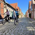 Zwei Radfahrer fahren auf einer gepflasterten Straße in der historischen Altstadt von Nienburg.
