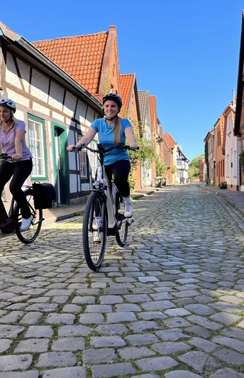 Zwei Radfahrer fahren auf einer gepflasterten Straße in der historischen Altstadt von Nienburg.