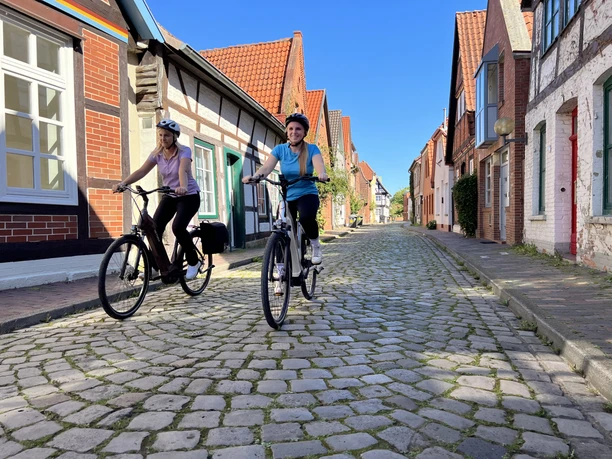 Two cyclists ride on a cobbled street in the historic old town of Nienburg.