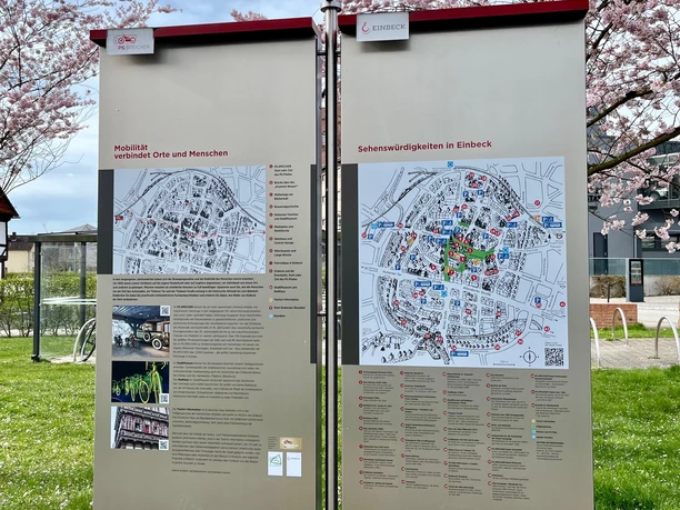 PS.Pfad, PS.SPEICHER, Frühling Zwei Informationstafeln des PS.Pfads in Einbeck mit Wegweisern unter rosa blühenden Bäumen.