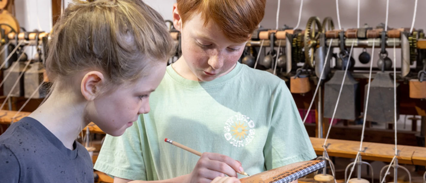 Familienführung Kritzelblock im LVR-Industriemuseum Textilfabrik Cromford, Ratingen Zwei Kinder stehen im LVR-Industriemuseum Cromford mit einem Notizblock vor historischen Webstühlen.
