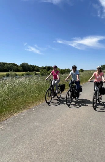 Drei Fahrradfahrer fahren auf einem ländlichen Weg unter blauem Himmel in der Mittelweser-Region.