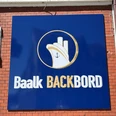 Baalk Backbord_1 Schild an einer Ziegelwand mit maritimem Logo und Schriftzug "Baalk Backbord" in Weiß auf Blau.Sign on a brick wall with maritime logo and lettering "Baalk Backbord" in white on blue.Skilt på en murstensvæg med maritimt logo og bogstaverne "Baalk Backbord" i hvidt på blåt.Bord op een bakstenen muur met maritiem logo en opschrift "Baalk Backbord" in wit op blauw.