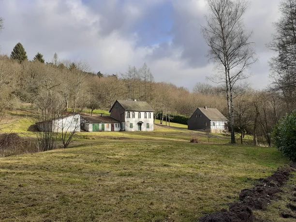 Grube Apfel im Volbachtal Drei historische Häuser in ländlicher Landschaft, umgeben von kahlen Bäumen unter bewölktem Himmel.