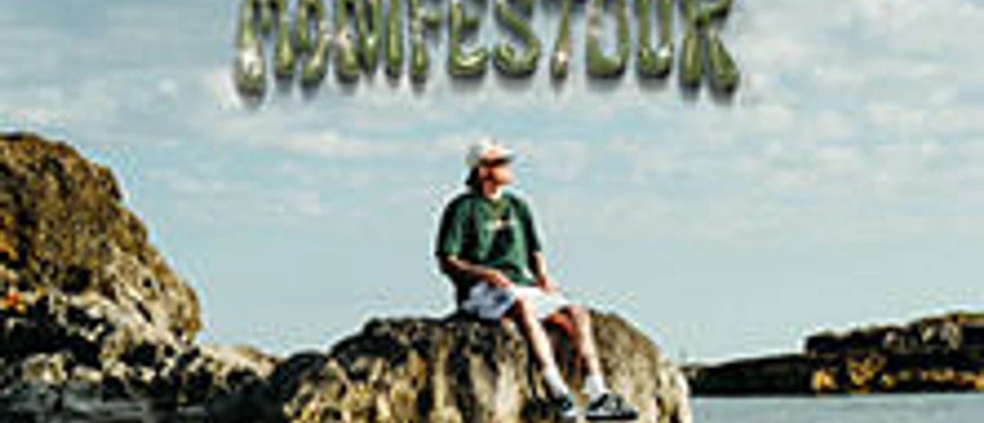 Ein Musiker sitzt auf einem Felsen am Wasser unter einem bewölkten Himmel mit der Aufschrift "ESTIKAY MANIFESTOUR".
